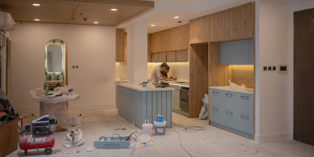 Cabinet - kitchen full remodel Two people discussing a full kitchen remodel near the sink, with under-cabinet lighting turned on and tools on the floor, illustrating a real renovation in progress.